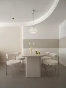 A modern dining room featuring a white dining table with a vase of flowers and fruits, surrounded by white seats, set against