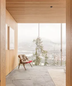 A modern interior space featuring wooden walls, rock flooring, and a red cushioned chair with natural fur, overlooking snowy 