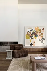 Modern living room featuring a comfortable brown fur chair, a large abstract artwork, and a coffee table with a book and bowl