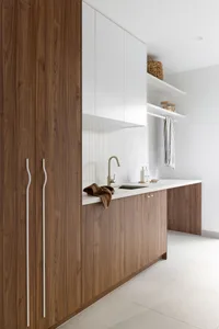 A modern minimalist kitchen featuring white countertops and wooden cabinets.