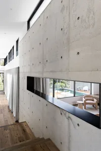 Minimalist living room with concrete walls, featuring a cozy seating area and a view of a swimming pool.
