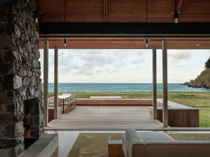 A modern residential deck overlooking the ocean with a stone fireplace and wooden flooring.