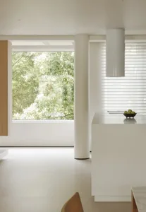 Modern minimalist interior with white materials, featuring a kitchen island with a bowl of green fruits, a window overlooking
