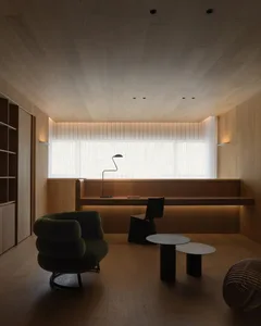 A minimalist living room with wooden elements and a concrete table, featuring a green armchair, a floor lamp, and a long tabl