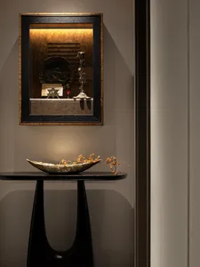 Black and gold framed mirror with metal sculpture and decorative elements on a black table with a floral arrangement.