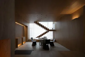 A modern interior space featuring wooden paneling, a staircase, and a dining area with a round table and chairs.