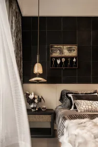 A modern bedroom featuring black tiles on one wall, a white bed with patterned pillows, and a glass pendant light hanging abo