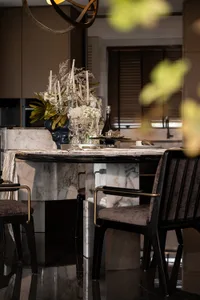 Modern dining room with marble materials, featuring a dining table, chairs, and decorative table setting with candles and flo