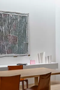 Modern dining room with wooden table and chairs, decorative rug, and abstract sculptures on a floating console.