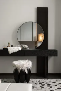 A modern interior design featuring a dressing table with a round mirror, black metal table, and a white faux fur stool on a p