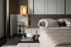 Modern minimalist bedroom featuring a bed with silver and gray pillows, a white and beige bedspread, and a side table with a 