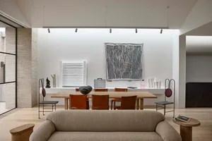 A modern minimalist living room featuring a wooden sofa, leather chairs, and stone elements.