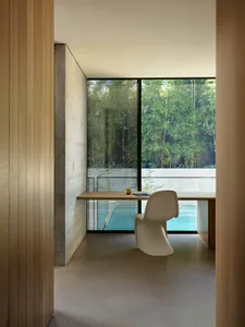 Minimalist office space featuring a concrete desk and chair with a large window overlooking a pool and greenery.