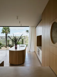 Modern residential interior with a kitchen island made of wood and a concrete countertop, featuring a view of the outdoors wi