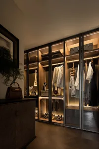 Modern walk-in closet with glass-panel walls, wooden shelving, and metal accents.