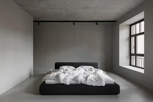 A minimalist bedroom featuring a grey concrete bed frame with white bedding, set against a grey concrete wall and floor.
