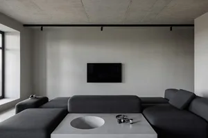 A minimalist living room with a dark gray sofa, a circular coffee table, and a wall-mounted flat-screen TV.