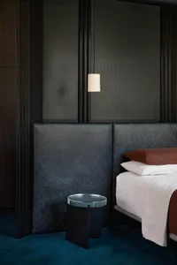 A modern bedroom featuring leather headboard, metal side table, and wooden floor.