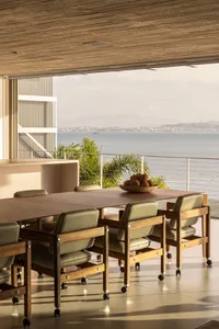 A minimalist dining room with wooden flooring, leather chairs, and a view of the sea.