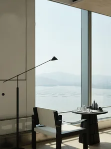 A modern living room featuring a sleek black chair with a white cushion, a small round table with a chess set, and a large wi