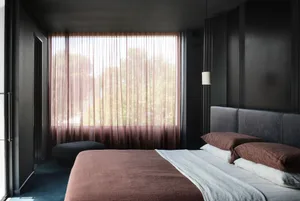 Modern minimalist bedroom with brown linens and a large window with sheer curtains.