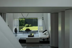 A minimalist living room with white marble accents and black furniture, featuring a large window with vertical blinds and a s