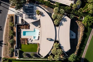 An aerial view of a modern residential house featuring a concrete exterior with a swimming pool and surrounding landscape.