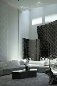 Modern interior design featuring taupe-colored fabric furniture, metallic accents, and a large window with a glass wall.