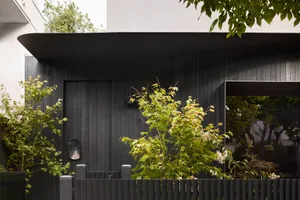 A minimalist residential exterior with a black door, green foliage, and a black fence.