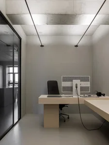 A minimalist office space with concrete walls, wooden furniture, and a desk with a computer setup.