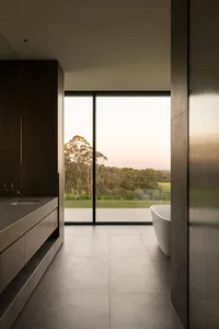 Modern bathroom with grey tiles and large glass window overlooking trees at dusk.