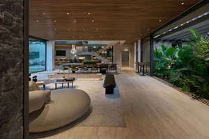 A modern living room with wooden flooring, furniture, and ceiling, featuring a large sofa, dining table, and plants.