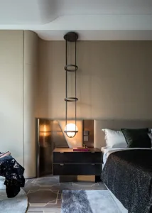 Modern minimalist bedroom with textured leather walls, hanging light fixture, black bedside table, and white bedding.