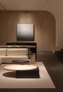 A modern minimalist living room features a white sofa, black tables, and a wooden panel wall.