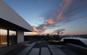 A rooftop deck with stone tiles, concrete surfaces, glass railings, and a beautiful sunset view.
