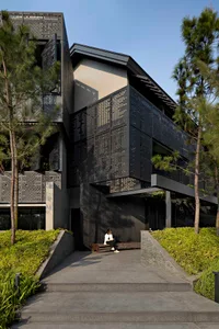 A modern house with a metal perforated panel facade, featuring black and white outdoor areas and lush greenery.
