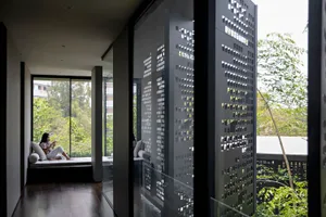 A modern interior space featuring a sleek, geometric steel panel wall, large windows providing natural light, and a serene ou