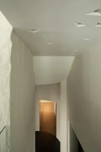 A corridor with minimalist design features, concrete walls, and geometric ceiling lights.