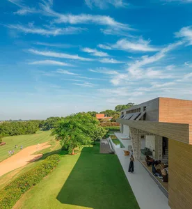 A modern residential exterior featuring glass walls and a stone foundation set against a blue sky with clouds.