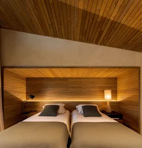 A modern bedroom with wooden walls and floors, featuring twin beds, nightstands, and lamps.