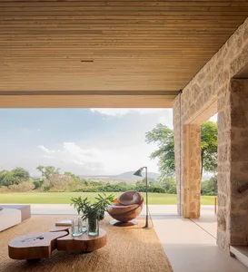 A modern living room with a wooden floor, stone walls, and glass windows, featuring a comfortable sofa, a unique coffee table