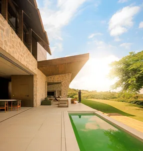 Modern villa with a stone exterior and a glass wall overlooking a green landscape.