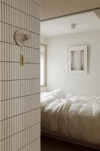 A minimalist bedroom with white tiled walls and a bed covered in white bedding.