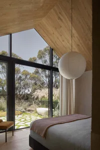 Modern minimalist bedroom with large windows overlooking a garden and a white spherical lamp hanging above the bed.