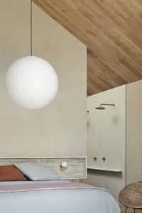 A minimalist bedroom with a white pendant light hanging above the bed, a wooden slanted ceiling, and ceramic tiles on the wal