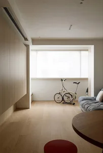 A minimalist living room with wooden flooring, a sofa, and a bicycle parked against a wall.