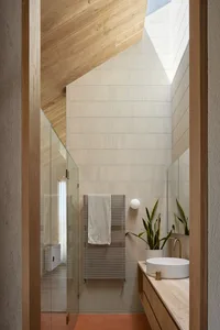 Modern bathroom with beige tiles, white sink, wooden accents, and a glass shower door.