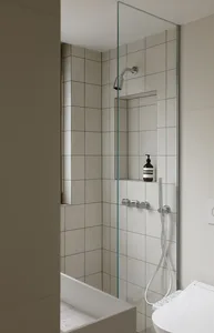 A modern bathroom featuring white tiled walls and a glass shower enclosure.