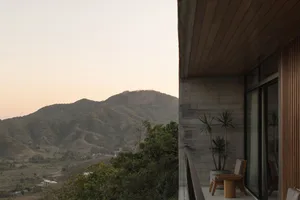 Concrete patio overlooking mountains with wooden furniture and plants on the side.