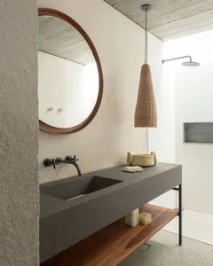Modern minimalist bathroom with a concrete countertop and sink, featuring a wooden shelf below and a circular mirror above.